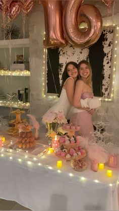 two women standing next to each other in front of a table filled with food and balloons