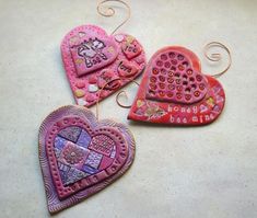 three heart shaped ceramic ornaments on a counter top, one is pink and the other is purple