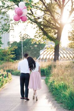 a man and woman are walking down a path in the park, one is wearing a pink skirt