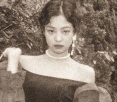 an old black and white photo of a woman holding something in one hand while standing next to some bushes