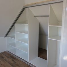 an empty room with white shelves and wooden flooring in the corner, under a slanted ceiling