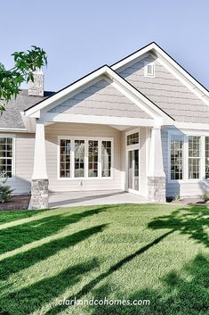 a gray house with white trim and windows on the front porch is surrounded by green grass