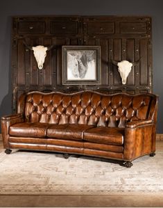 a brown leather couch sitting in front of a wooden wall with two steer heads on it