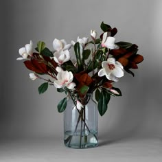 a vase filled with white flowers on top of a table next to a gray wall