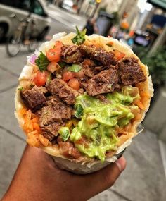 a person holding up a burrito with meat and guacamole on it