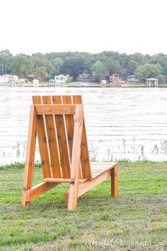 a wooden bench sitting on top of a lush green field next to a lake with houses in the background