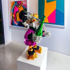 a colorful glass sculpture on top of a white pedestal in front of a brightly colored painting