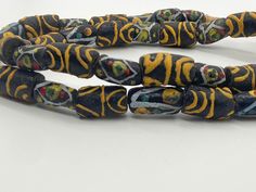 Antique Venetian Black African Trade Beads with beautiful Ethnic African Pattern design in yellow, light blue, white, red, and green.  The beads are handmade, each bead is unique, and they are rare. There are a few imperfections throughout the beads due to the fact they're handmade and old. Sizes, conformity and colors vary.  You will receive the strand shown in the pictures. The strand is about 68cm/27" long. Bead sizes vary.  If you have additional questions about this item, please don't hesit Large Yellow Beads For Festivals, Yellow Large Beads For Festivals, Artisan Yellow Beads For Festivals, Artisan Yellow Beaded Necklaces For Festivals, Traditional Yellow Beaded Necklaces With Polished Beads, Traditional Yellow Beaded Necklace With Polished Beads, Traditional Yellow Beaded Necklace For Festivals, Ceremonial Multicolor Beaded Necklaces With Round Beads, Yellow Polished Beads For Festivals