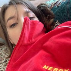 a woman laying on top of a couch covered in a red jacket with the word nerdy written on it