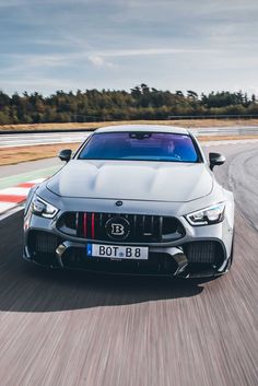 the front end of a silver sports car driving on a track with trees in the background