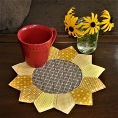 a coffee cup sitting on top of a table next to a vase filled with yellow flowers