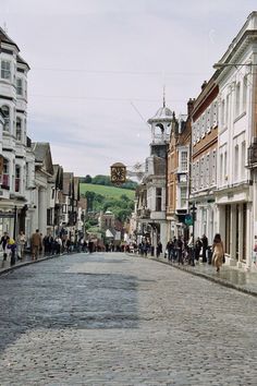 a cobblestone street lined with buildings and people walking on the sidewalks in front of them