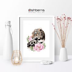 a white vase with pink flowers next to a framed print of a leopard on it