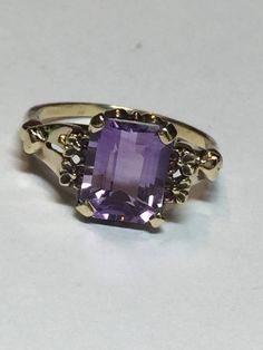 This is a beautiful ring marked 10k. It is yellow gold with a prong set 9x7mm rectangular genuine faceted amethyst. On either side of the stone is 2 floral accents. This has a great design. It weighs 2.4 grams. It is a ring size 5.75 and could be sized for an additional fee if needed. This ring is in great vintage condition. Any questions, please email me. 14k Gold Purple Emerald Cut Rings, Purple 14k Gold Ring With Emerald Cut, Purple 14k Gold Rings With Emerald Cut, Classic Yellow Gold Rectangular Amethyst Ring, Vintage Emerald-cut Amethyst Ring For Anniversary, Rectangular Amethyst Ring In Yellow Gold, Vintage Emerald Cut Amethyst Ring For Anniversary, Yellow Gold Amethyst Ring With Rectangular Shape, Formal Purple Amethyst Ring With Rectangular Shape