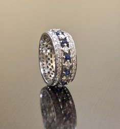 DeKara Designs Collection A three row diamond and Ceylon blue sapphire eternity band made in 18K white gold. Metal- 18K White Gold, .750 Stones- 94 Round Diamonds, F-G color VS1-VS2 clarity, 1.12 Ct, 12 Round Ceylon Blue Sapphires, 0.30 Carats. Art Deco Style Vintage Inspired Ceylon Blue Sapphire Eternity Diamond Engagement Band Made in 18K White Gold. This unique eternity band features both prong and pave stone setting. There are alternating prong set diamonds and blue sapphires in the center o Anniversary Sapphire Wedding Ring With Single Cut Diamonds, Sapphire Jewelry With Single Cut Diamonds For Wedding, Silver Sapphire Ring With Pave Setting For Wedding, Sapphire Eternity Band With Brilliant Cut For Wedding, Diamond Eternity Band With Sapphire For Wedding, Sapphire Diamond Eternity Band For Wedding, Wedding Sapphire Ring With Pave Setting, Brilliant Cut Sapphire Eternity Band For Wedding, Anniversary White Gold Sapphire Ring With Pave Setting