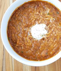 a white bowl filled with chili and sour cream on top of a wooden table next to a spoon