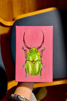 a painting of a green beetle on a pink background, with red antlers and horns