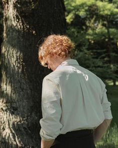 a woman standing in front of a tree with her back turned to the camera, wearing a white shirt and black skirt