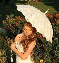 a beautiful young woman holding an umbrella in her hand while standing next to some flowers