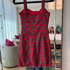 a red and black plaid dress hanging on a clothes rack in front of a mirror