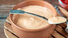 a spoon is sitting in a bowl with peanut butter on it and tomatoes behind it