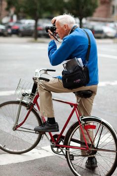 an old man riding a bike while holding a camera