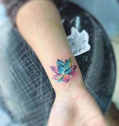 a woman's wrist tattoo with a colorful lotus flower on the left side of her arm