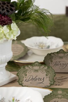 there are place cards on the table with flowers in vases and plates next to each other