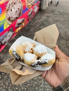 a hand holding a paper plate filled with powdered sugar covered donuts