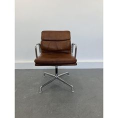 a brown leather office chair sitting on top of a cement floor next to a white wall