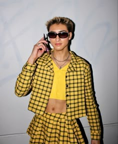 a woman in yellow and black checkered outfit holding a cell phone to her ear