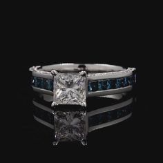 a princess cut diamond ring with blue sapphires on the sides and channeled band