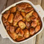 a white casserole dish filled with bread and cinnamon rolls on top of a wooden table