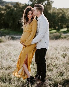 a pregnant couple standing in the middle of a field