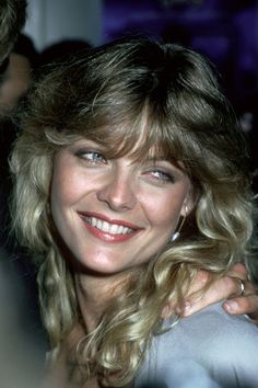 a woman with blonde hair smiling and hugging another woman's shoulder at an event