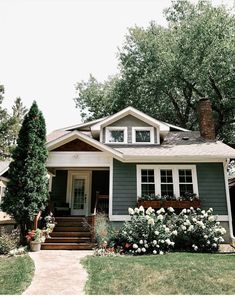 a gray house with white trim and flowers in the front yard