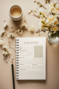 the game review book is next to a cup of coffee and some white flowers on a table