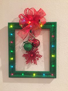 a christmas ornament hanging on the wall in a green frame with lights around it