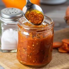 a spoon full of chili sauce sitting on top of a wooden cutting board