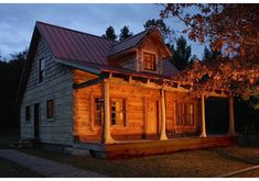 a small wooden house lit up at night with lights on the porch and covered porch