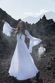 a woman in a white dress is standing on the ground with her arms outstretched and holding a lantern