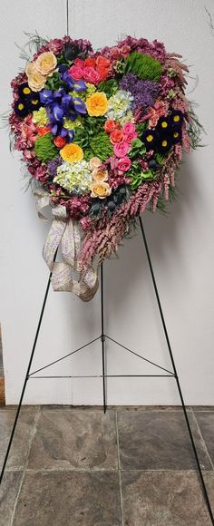 a heart - shaped arrangement of flowers is placed on a easel in front of a wall