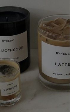 two candles sitting next to each other on top of a white counter with brown labels