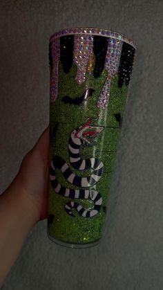 a hand holding a green and black tumbler with an image of a snake on it