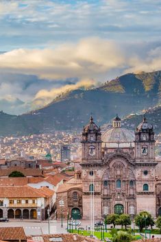 an old building in the middle of a city with mountains in the background and clouds in the sky