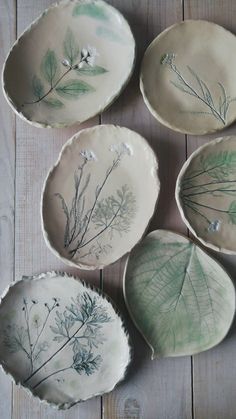 four plates with plants painted on them sitting on a wooden table next to each other