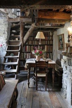 a room with a table, bookshelf and stairs leading up to the second floor