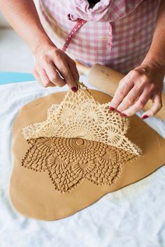 a woman is working on an art project with clay and crocheted doily