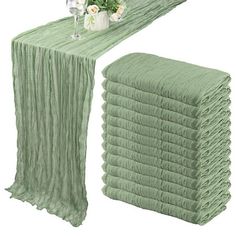 a stack of green cloths next to a vase with flowers on it and a table runner