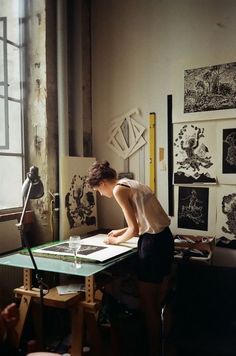 a woman is writing on a piece of paper at a desk in an art studio